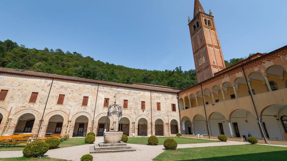A historic courtyard with a tall tower, arched walkways, and a central fountain.