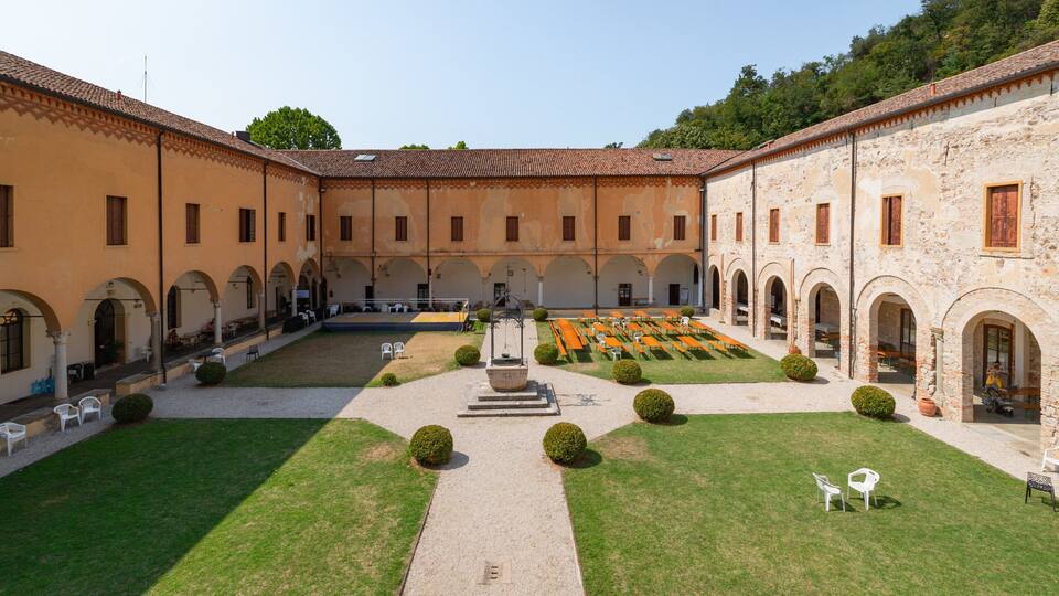 A courtyard with a central fountain, surrounded by buildings with arched windows and a tiled roof.