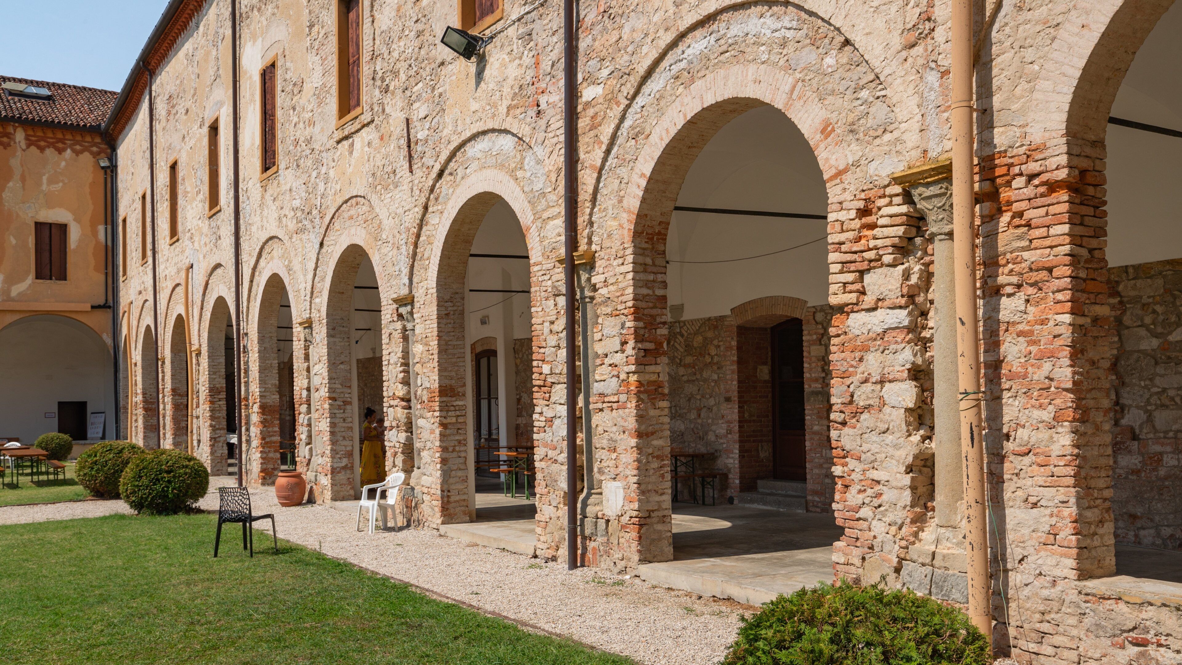A courtyard with stone arches, a grassy area, and a building with a tiled roof.
