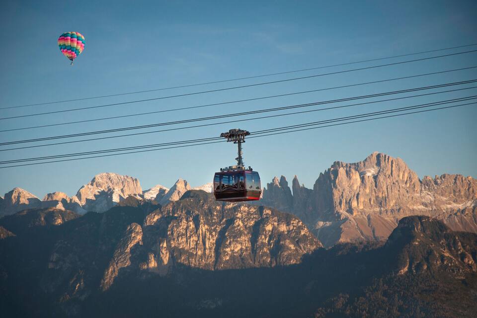 A cable car ascending a mountain with a colorful hot air balloon in the background.