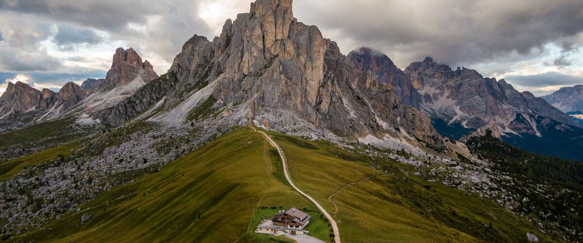A mountain landscape with a prominent rocky peak, a winding path leading to a small building, and surrounding green hills.