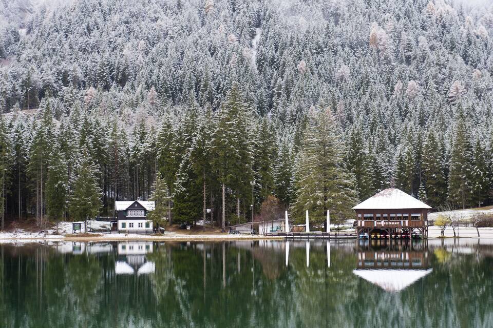 A cabin and a restaurant by a calm lake, surrounded by snow-covered trees.