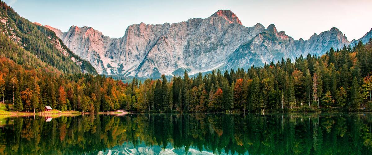 A mountain range reflected in a calm lake with autumn-colored trees.