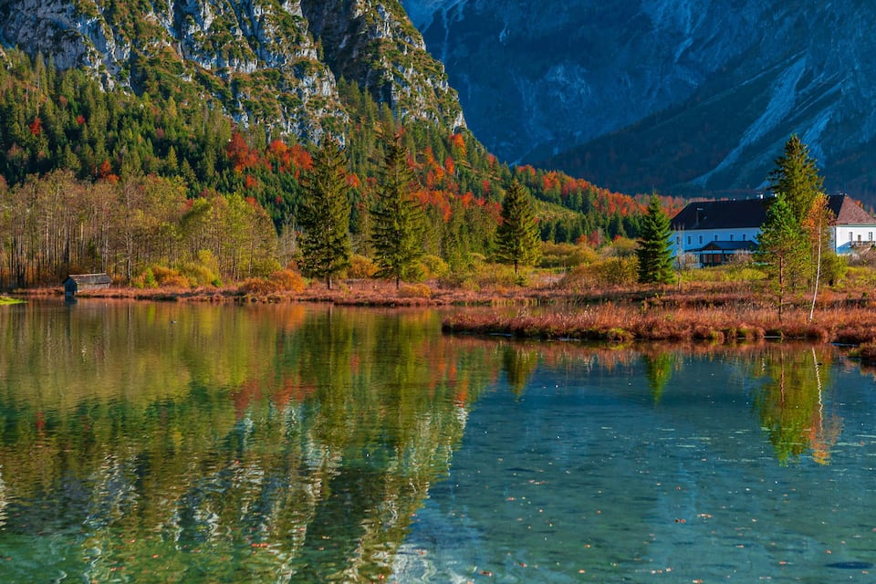 A mountain lake with clear reflections, autumn-colored trees, and a house in the foreground.