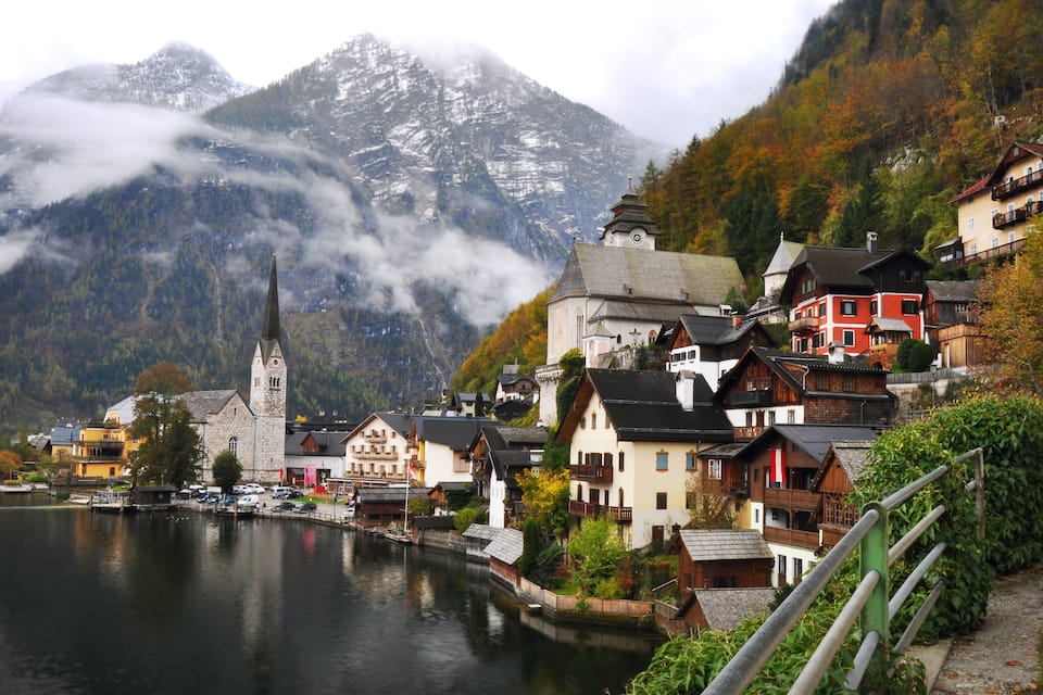 A lakeside village with traditional houses, a church, and mountains in the background.