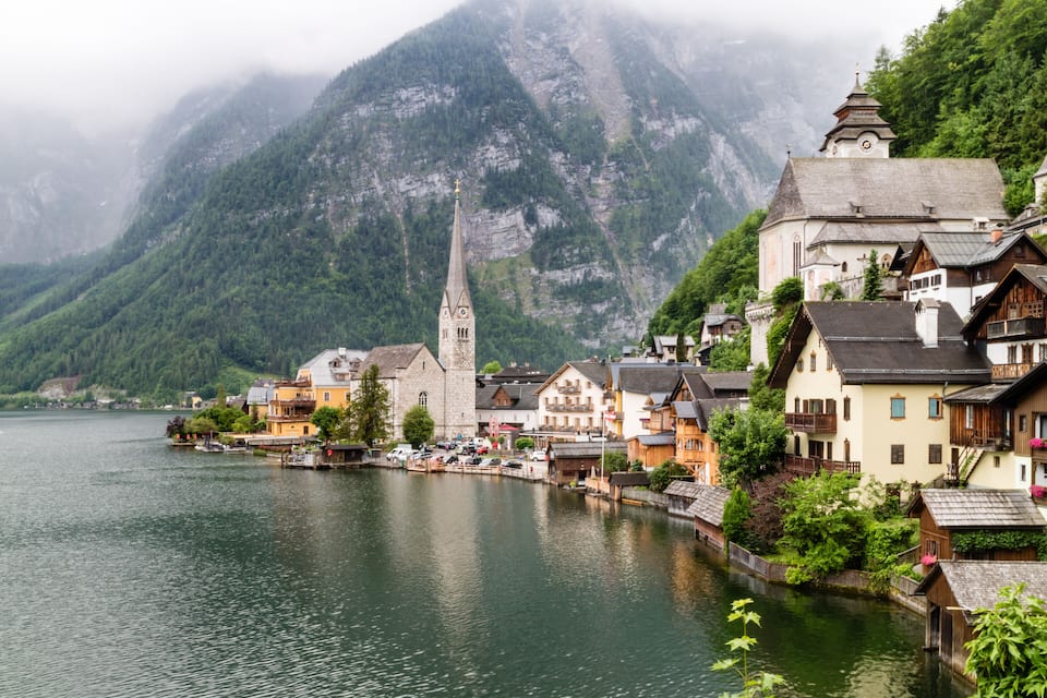 A lakeside village with traditional buildings, a church, and a mountain backdrop.