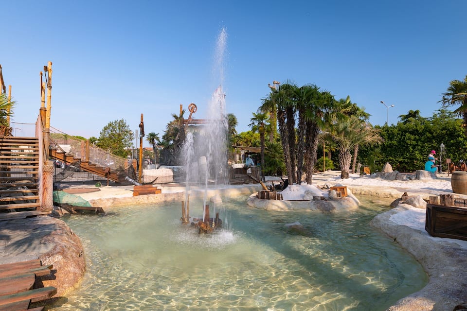 Een drinkwaterfontein omringd door rotsen en palmbomen.