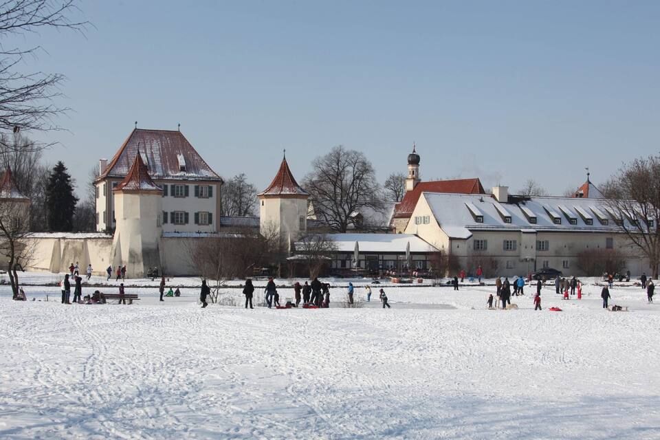 A snow-covered park with historic buildings and people engaging in winter activities.
