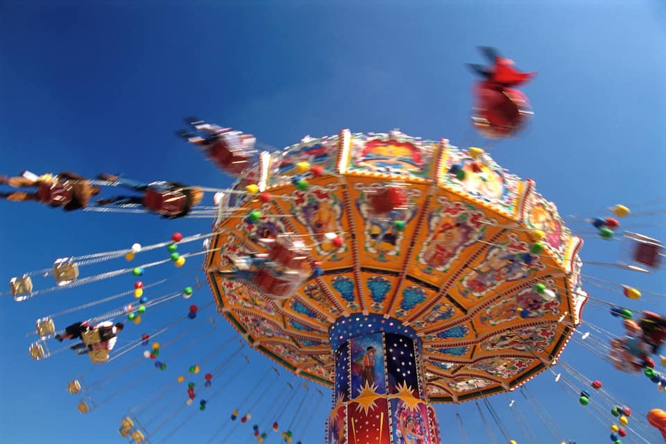 A colorful carousel with a blue and red striped pole, surrounded by a clear blue sky.