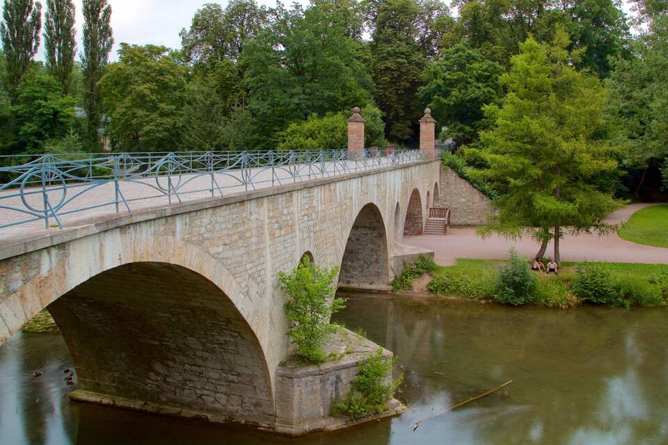 Eine Steinbrücke über einem Fluss, umgeben von Bäumen und Grün.