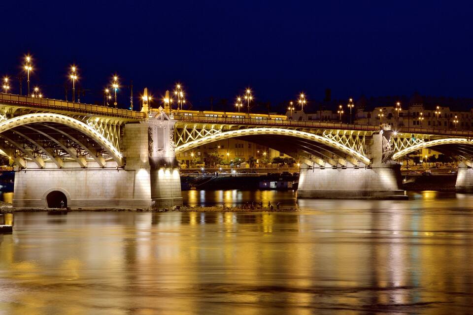 A brightly lit bridge with two arches over a river at night.