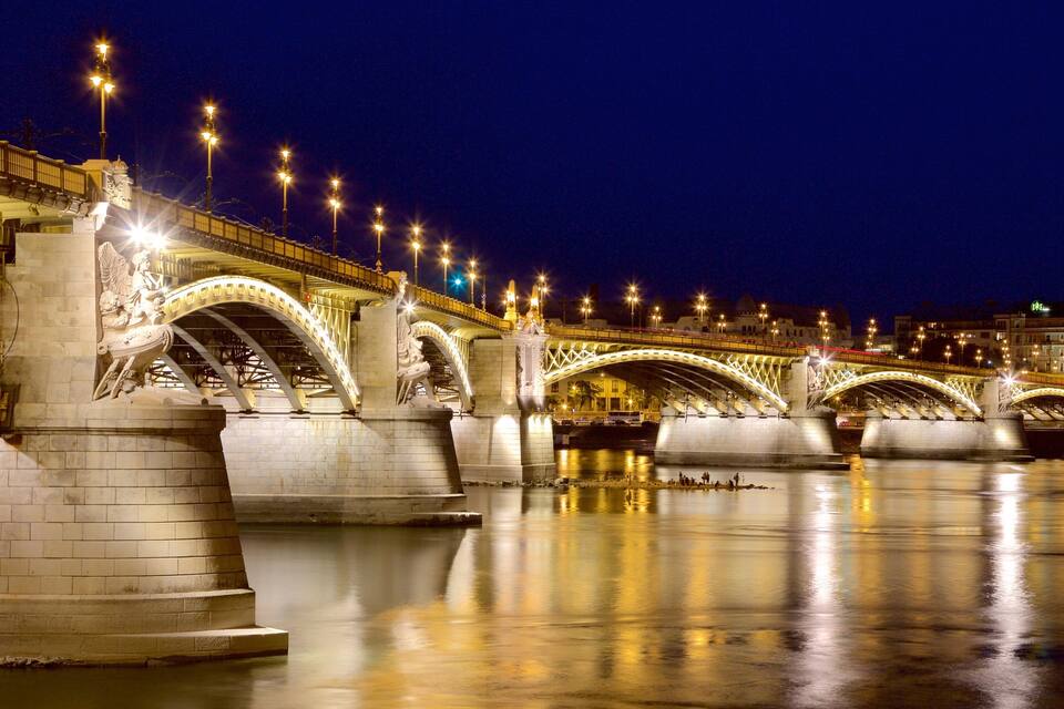 A brightly lit bridge with multiple arches over a calm river at night.