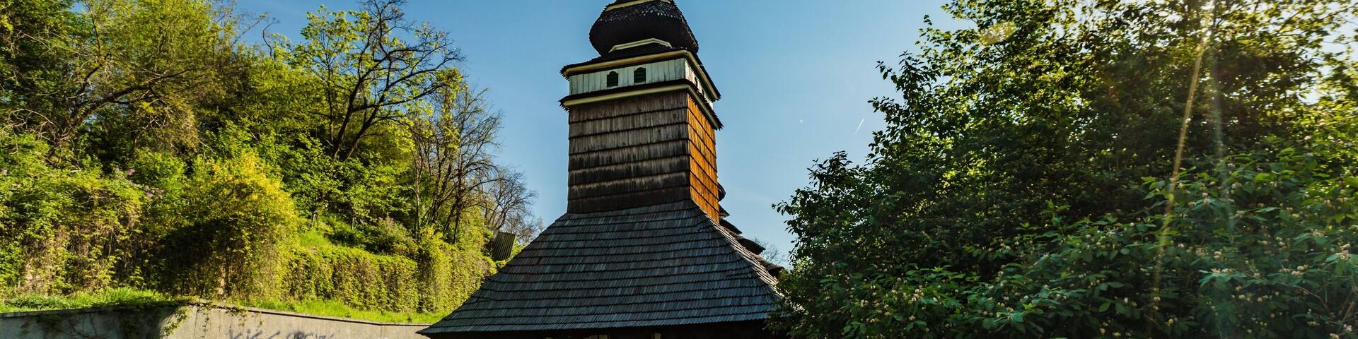 Prague, Czech Republic - April 22 2019: Church of the Archangel Michael built in 18th century with shingled roof, made of wooden logs standing at Kinsky garden. Sun shining through green bush.