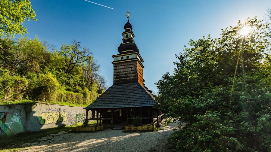 Prague, Czech Republic - April 22 2019: Church of the Archangel Michael built in 18th century with shingled roof, made of wooden logs standing at Kinsky garden. Sun shining through green bush.