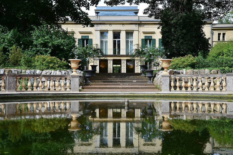 A classical building with columns, a reflecting pool, and a stone balustrade.