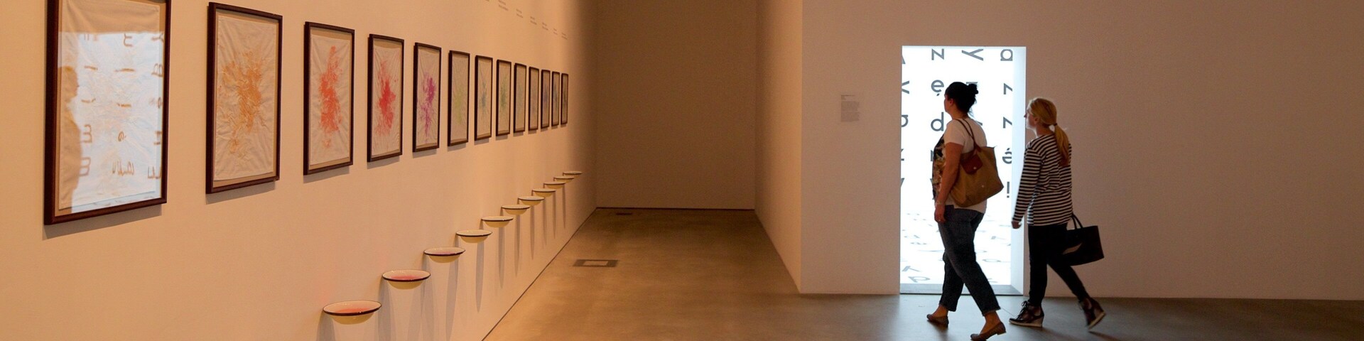 Uma galeria de arte com um corredor comprido exibindo obras de arte emolduradas na parede esquerda.