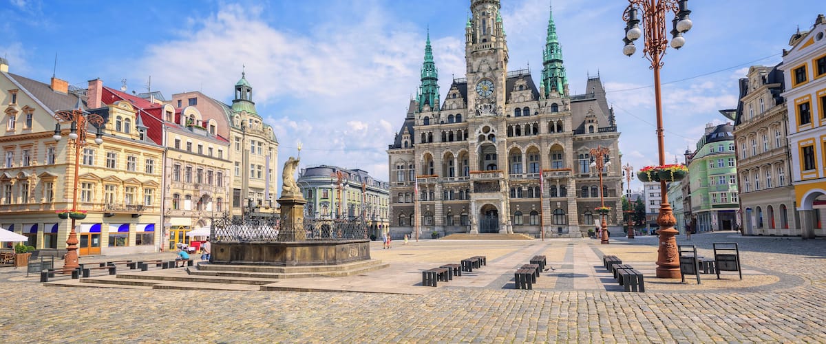 A historic square with a prominent church featuring twin spires, cobblestone pavement, and surrounding colorful buildings.