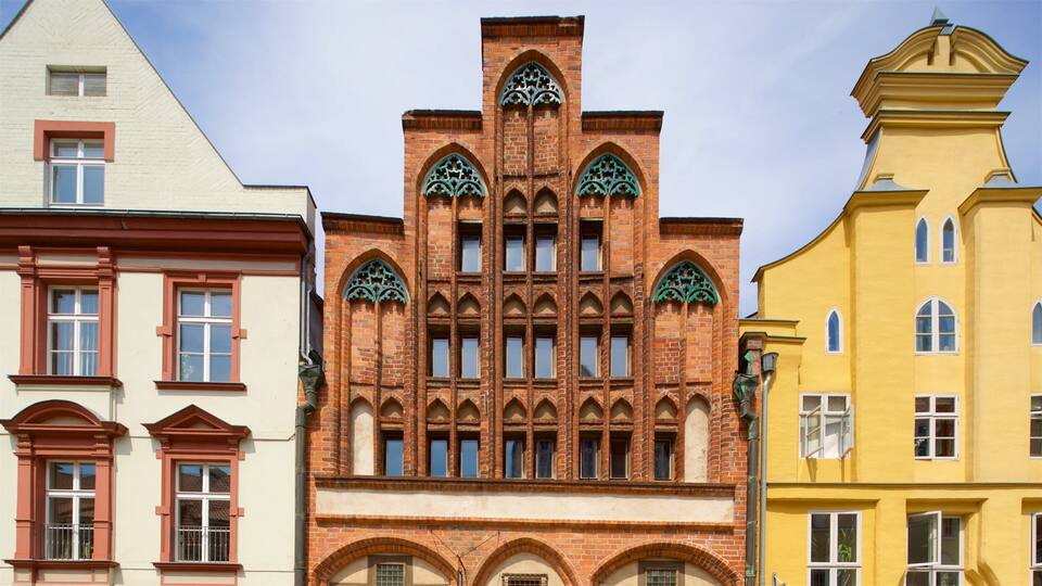 Una hilera de edificios coloridos con estilos arquitectónicos distintos, incluyendo una construcción de ladrillo rojo con arcos apuntados y marcos de ventanas verdes.