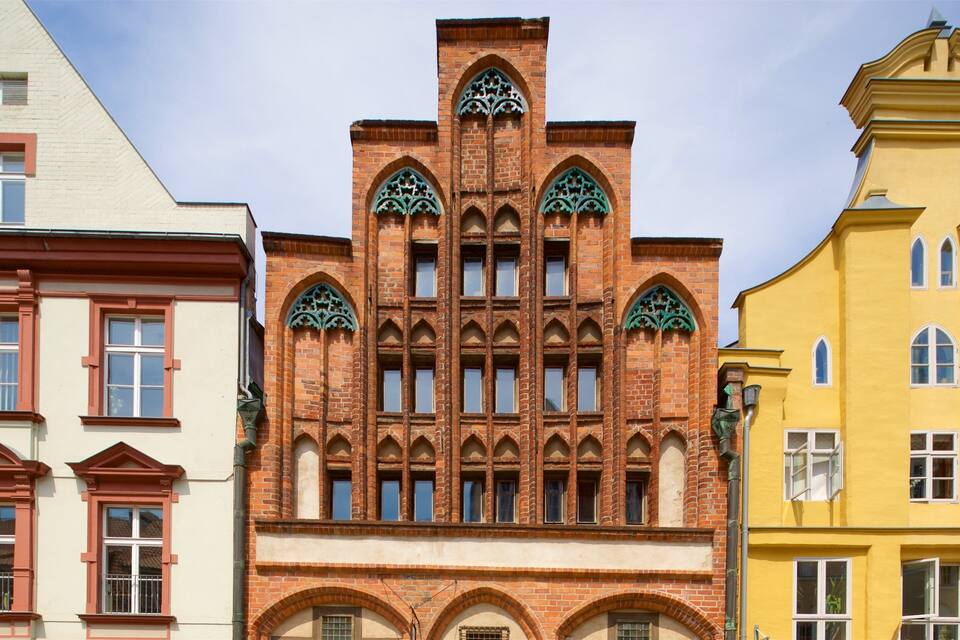 Una hilera de edificios coloridos con estilos arquitectónicos distintos, incluyendo una construcción de ladrillo rojo con arcos apuntados y marcos de ventanas verdes.