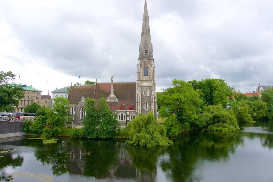 Een historische kerk met een hoge spits, omringd door weelderige begroeiing en een rustige rivier.