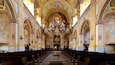 An ornate church interior with high ceilings, detailed frescoes, and a central chandelier.