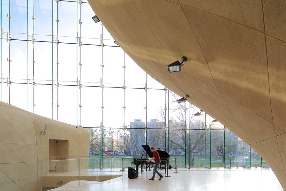 A modern building with large glass windows and a piano in the center.