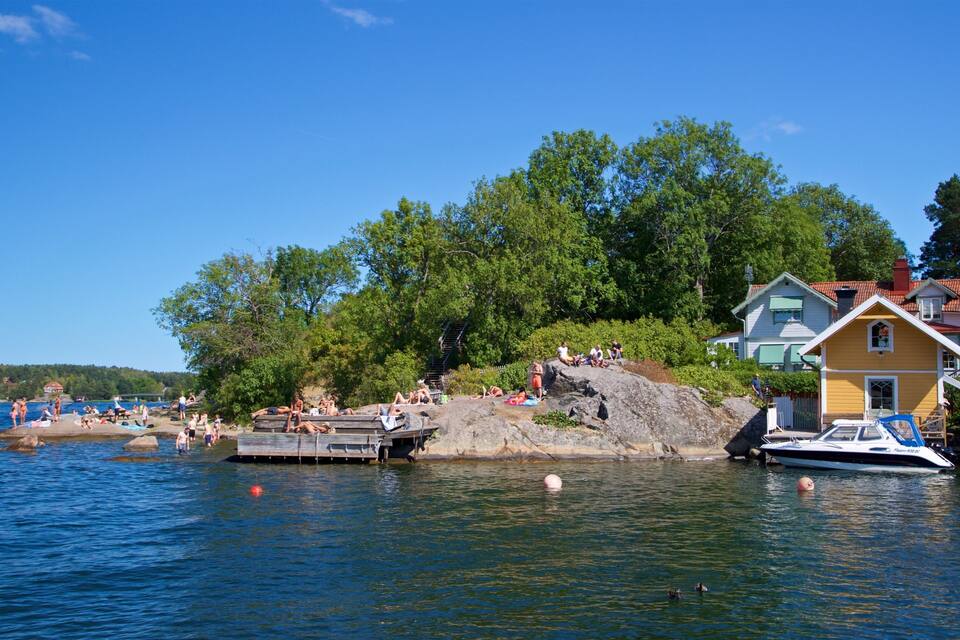 En vy över en sjö med en brygga, ett gult hus och en båt.