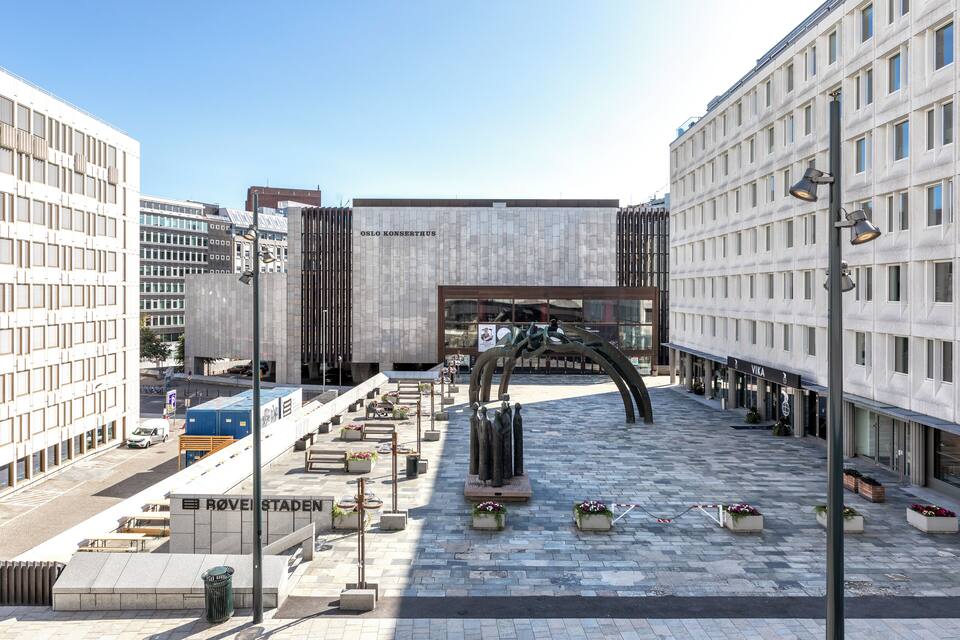 Una plaça amb un edifici modern anomenat 'OSLO KONSERTHUS' i una escultura al centre.