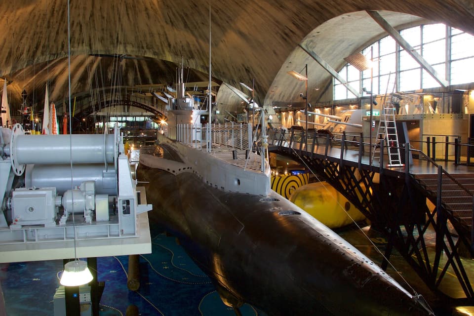 En stor ubåt visas i ett museum inomhus, med ett högt, välvt tak och stora fönster.