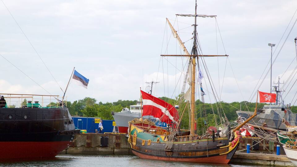 A historic sailing ship docked at a harbor with other vessels and a flag.