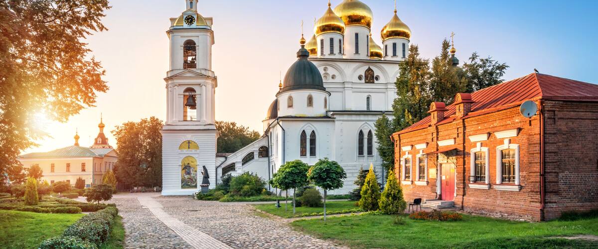 A church with golden domes and a bell tower, surrounded by a cobblestone path and greenery.