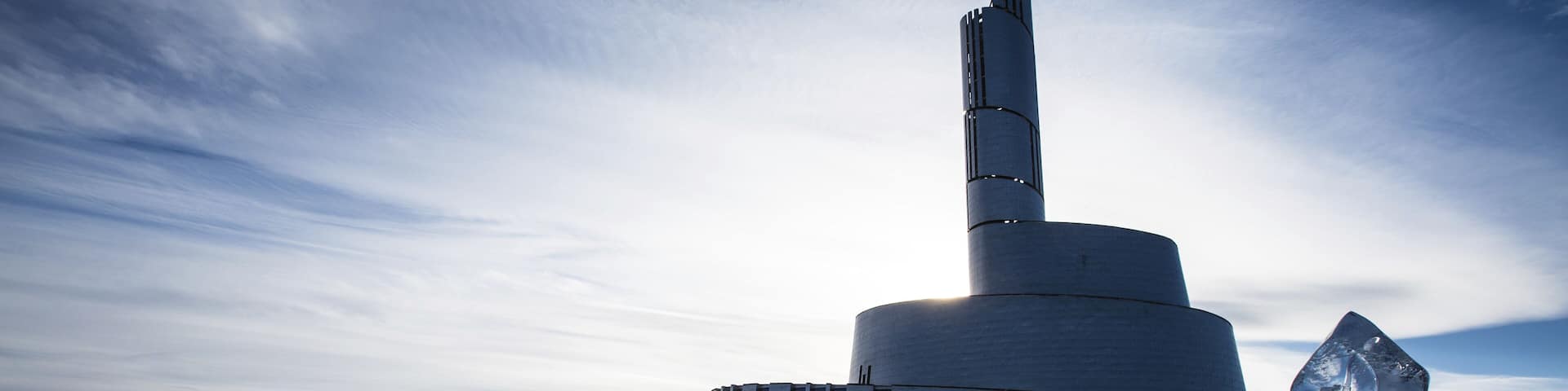 A modern building with a cylindrical base and a tall, slender tower.