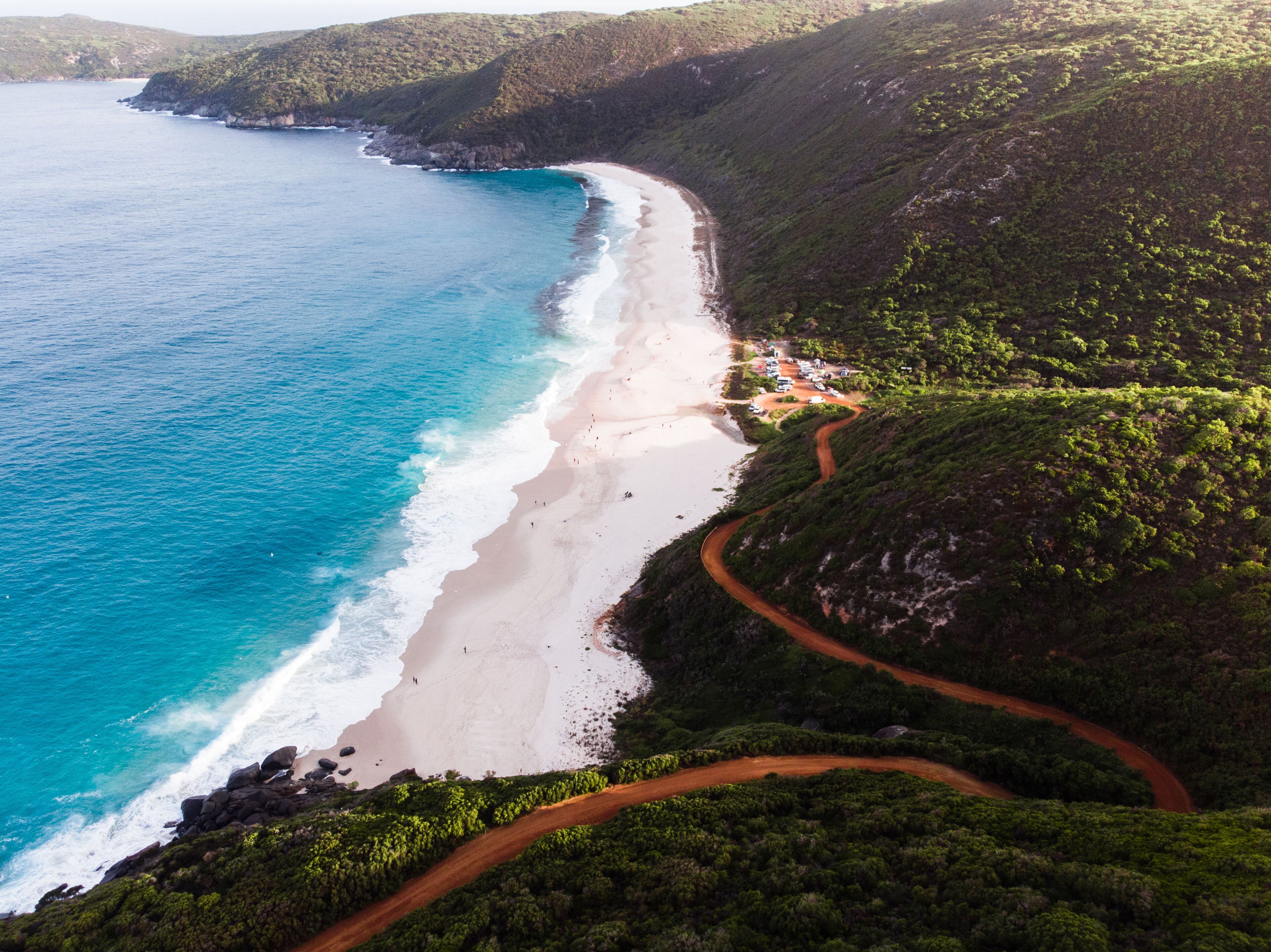 A coastal landscape with a winding road, a beach, and lush green hills.
