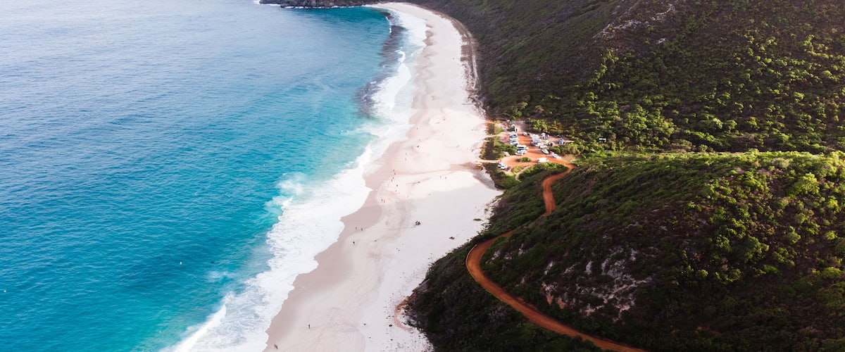 A coastal landscape with a winding road, a beach, and lush green hills.