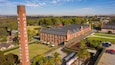 Chateau Thundra, een groot bakstenen gebouw met een opvallende schoorsteen, omgeven door weelderige begroeiing en een verzorgd gazon.