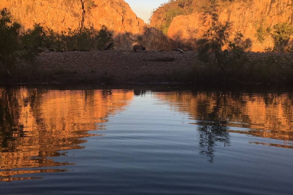 A calm river reflecting the surrounding cliffs and sparse vegetation.
