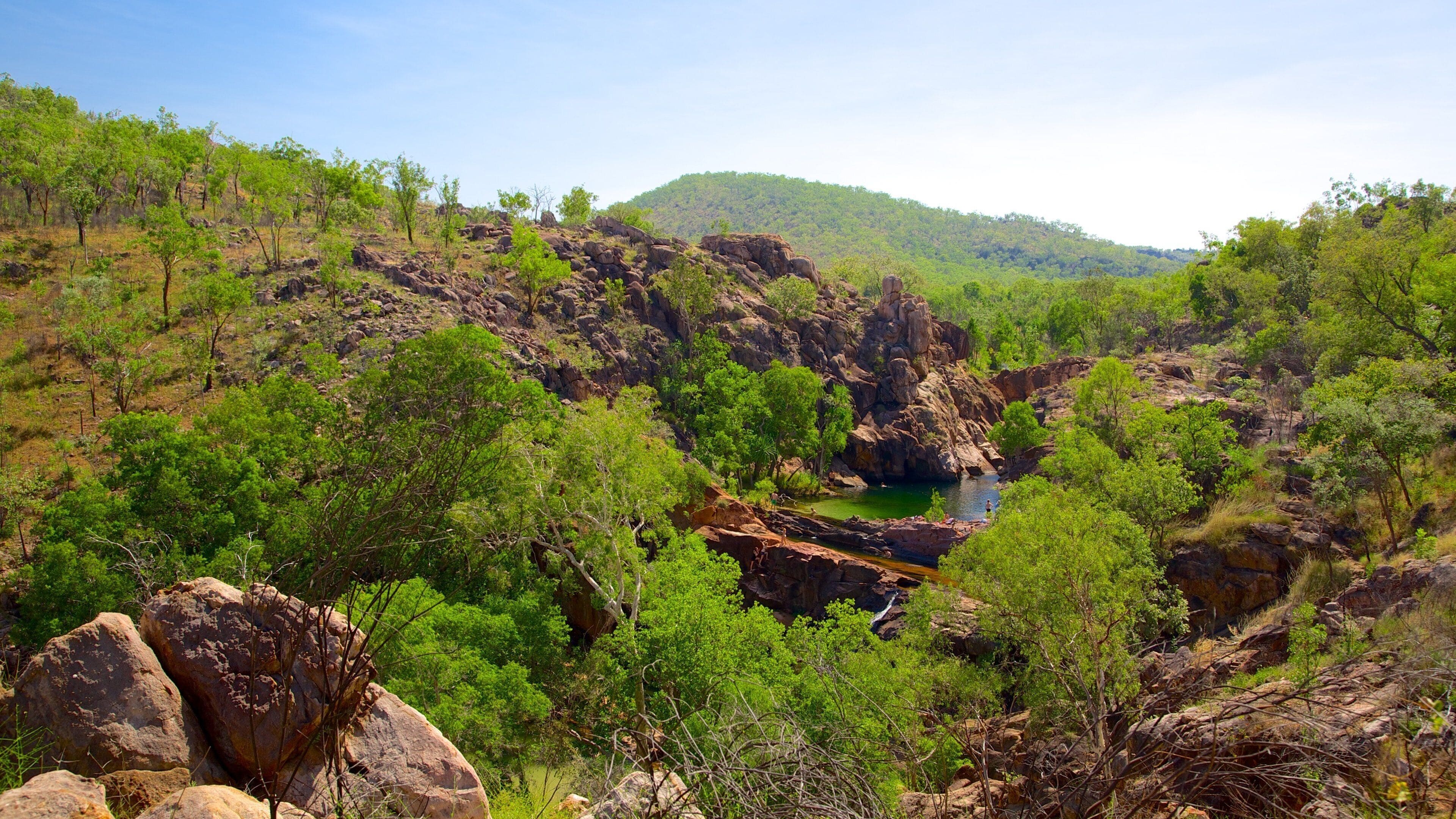 Un canyon rocheux traversé par une petite rivière, entouré d’arbres verdoyants et de collines.