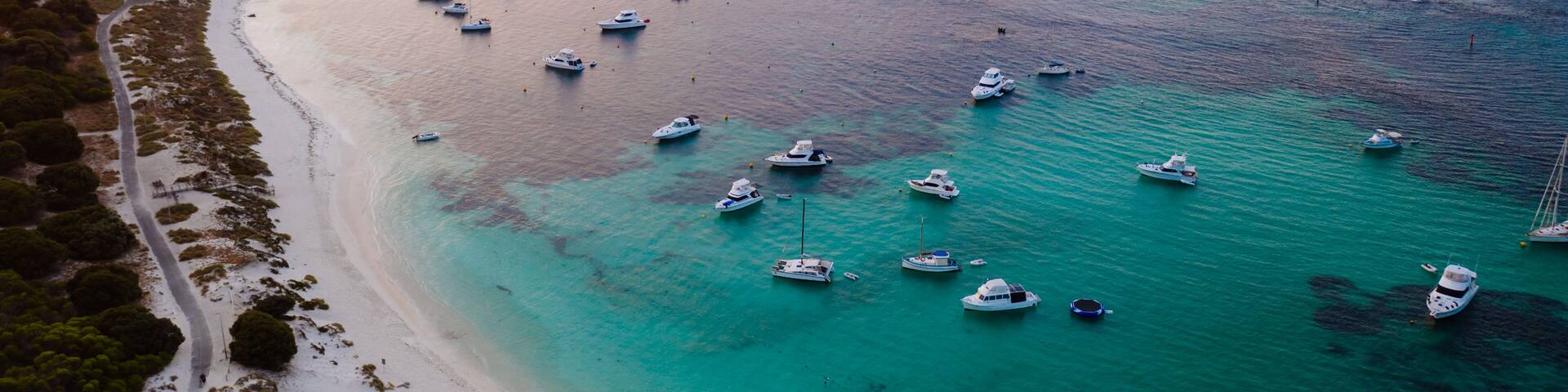 A coastal area with a sandy beach, boats anchored in the water, and a rocky outcrop in the distance.