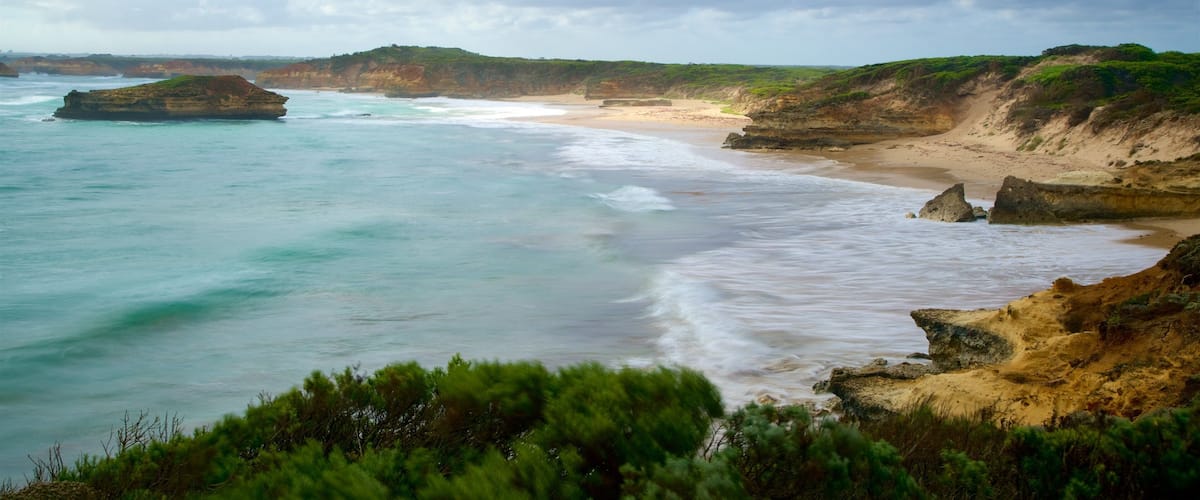 A coastal landscape with a sandy beach, rocky cliffs, and turquoise waters.