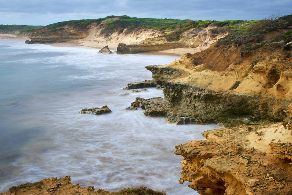 A coastal landscape with a sandy beach, rocky cliffs, and a turbulent sea.