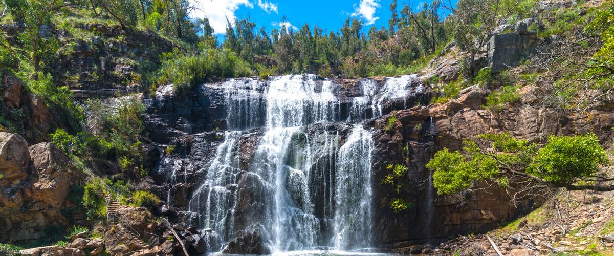 A multi-tiered waterfall cascading into a pool surrounded by rocky terrain and sparse vegetation.