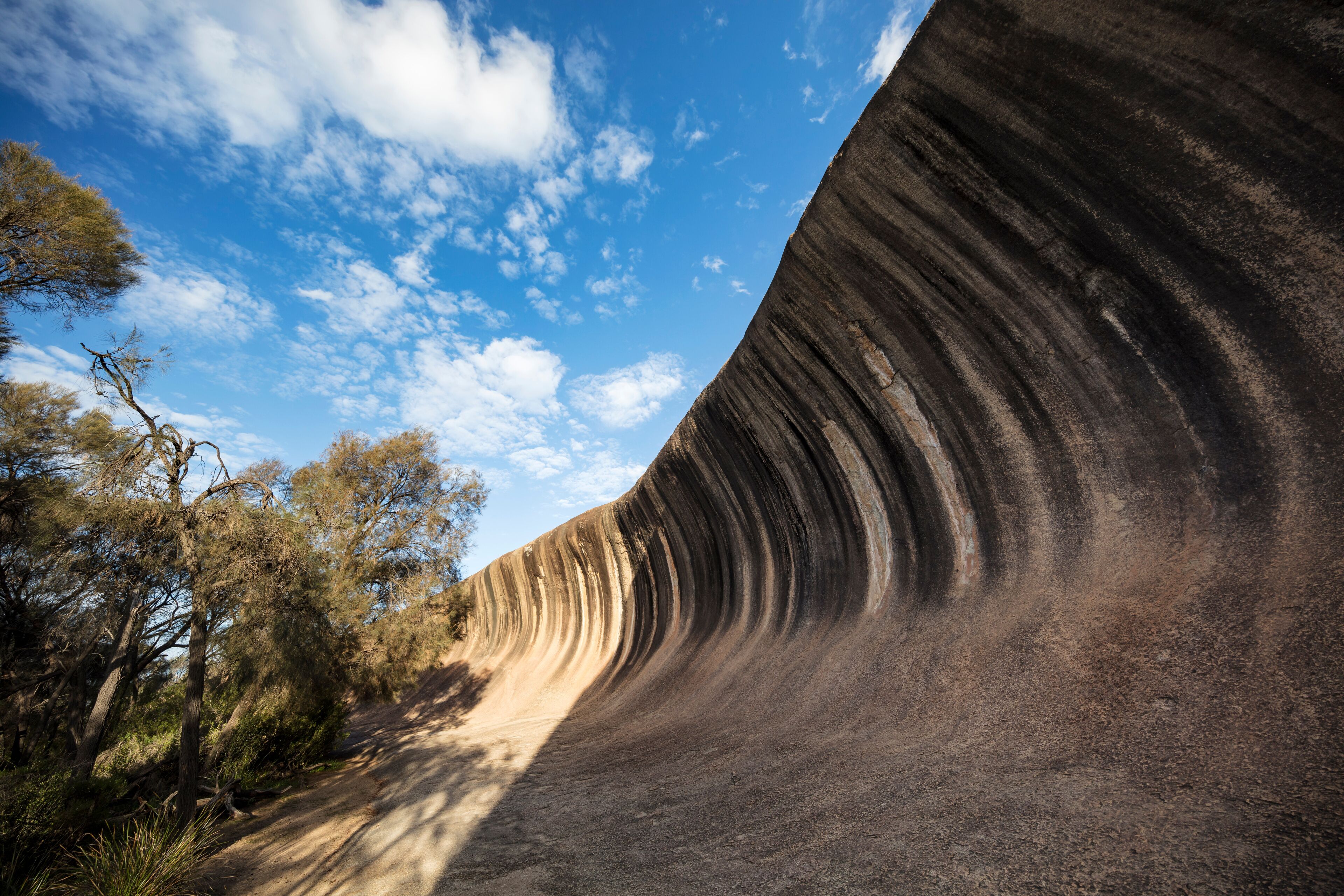 A large rock formation with a curved overhang, surrounded by trees and a clear blue sky.