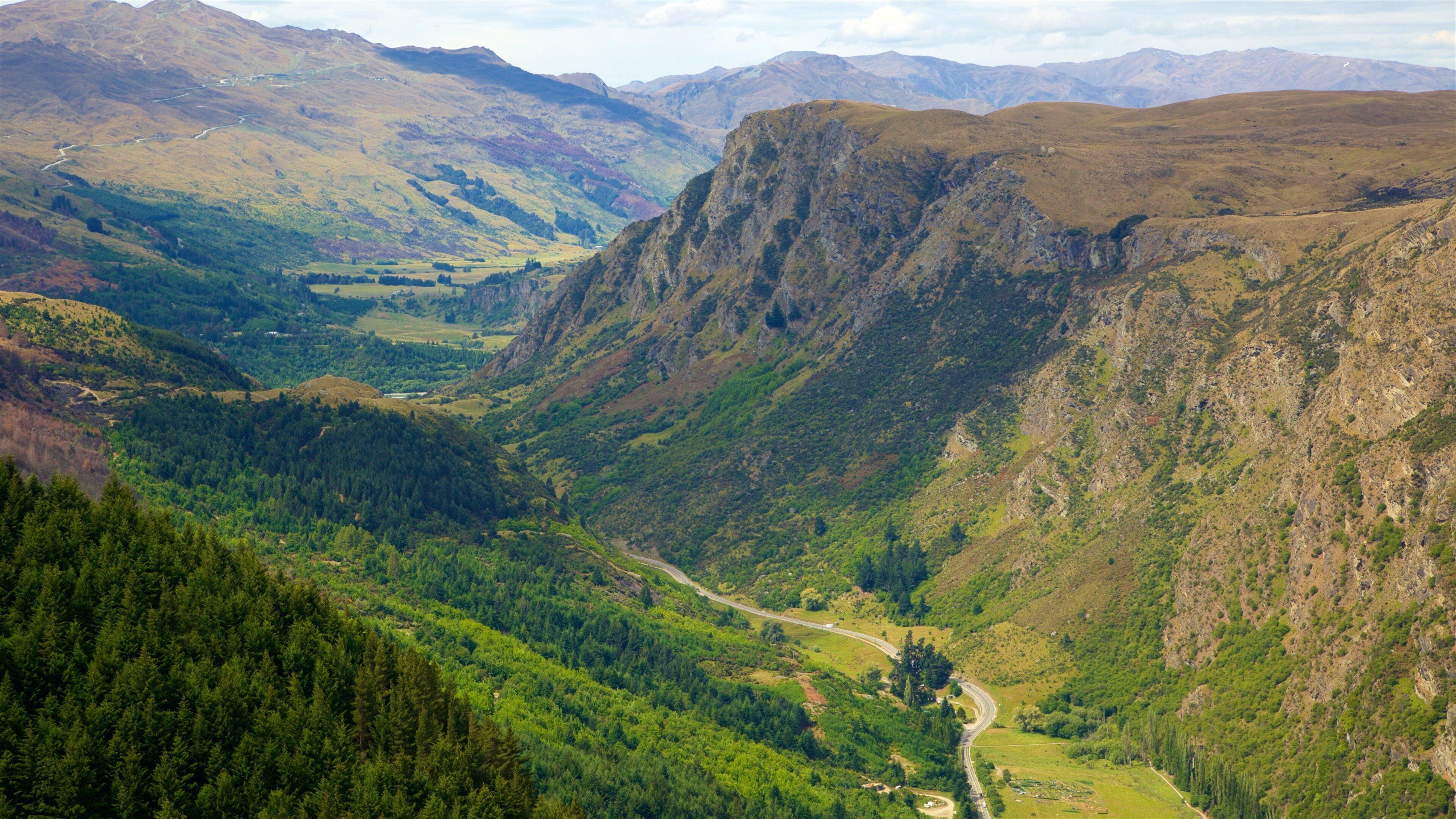 A valley with a winding road, dense forests, and rugged mountains.