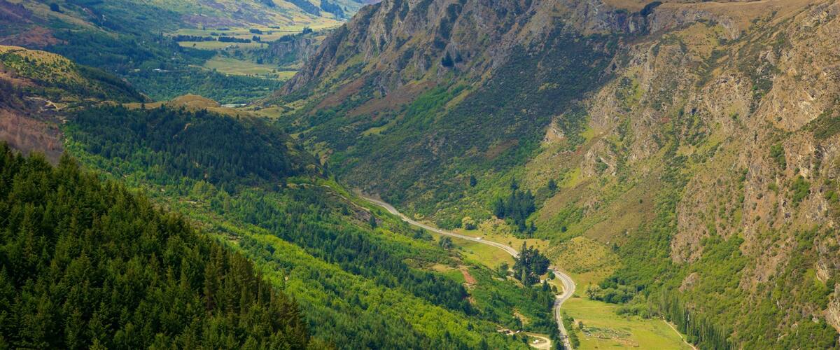 A valley with a winding road, dense forests, and rugged mountains.