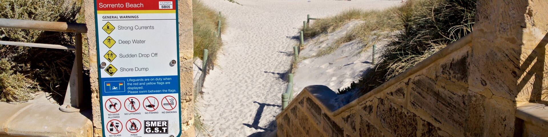 A beach entrance sign with warnings and regulations.