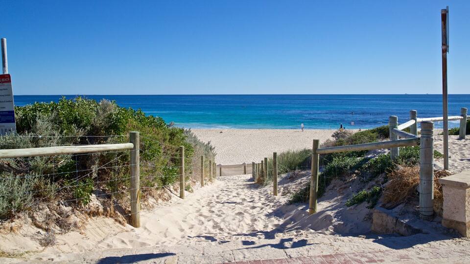 Un sentier sablonneux qui longe la plage et mène à une étendue d’eau bleue et limpide.