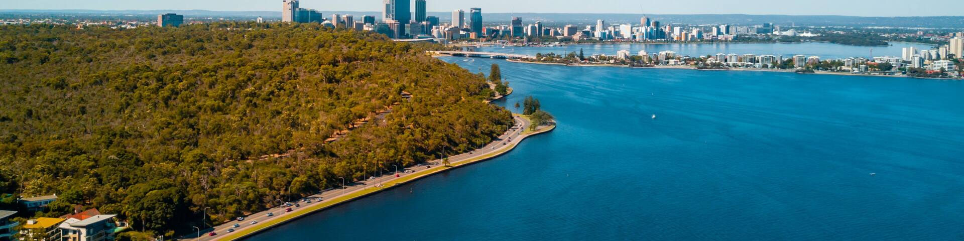 Una ciudad costera con una densa área boscosa, un puerto deportivo y un horizonte de edificios modernos.