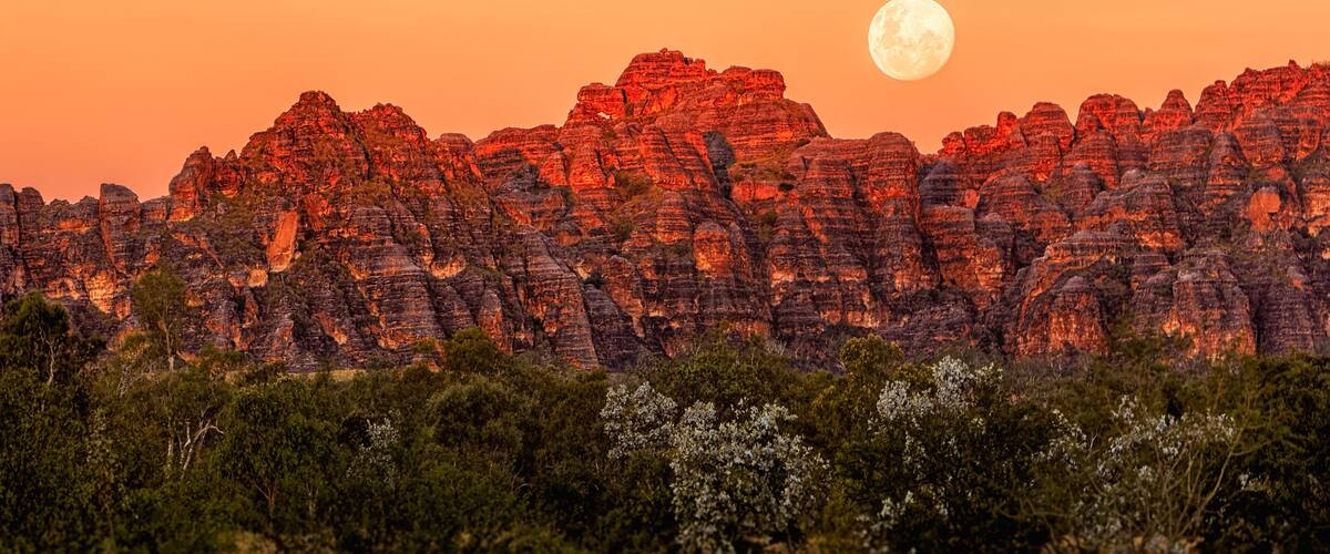 A mountain range with a full moon in the sky.