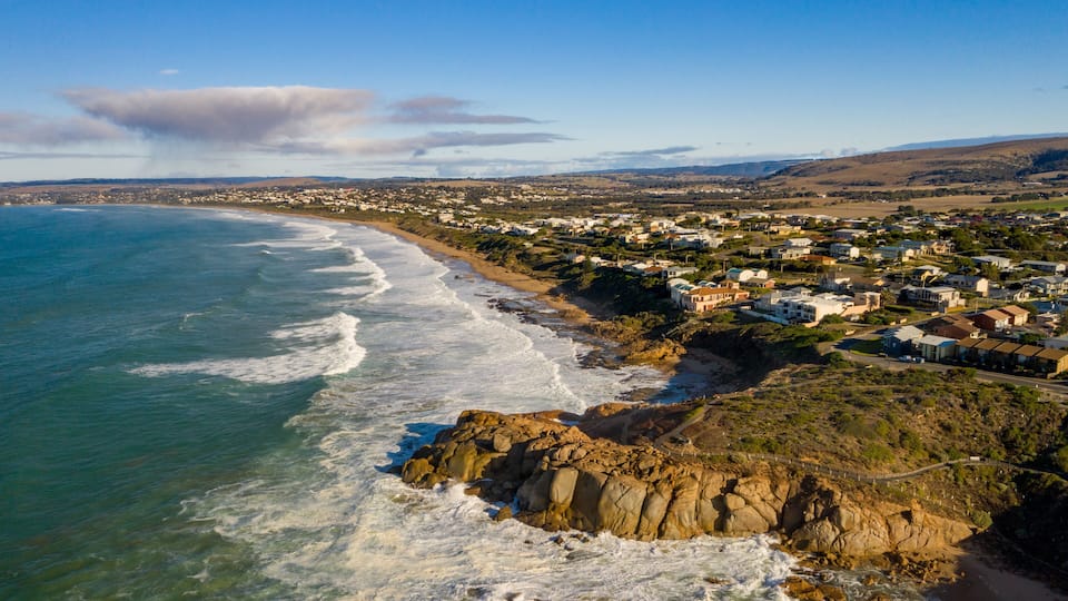 A coastal town with a beach, rocky shoreline, and houses along the coast.