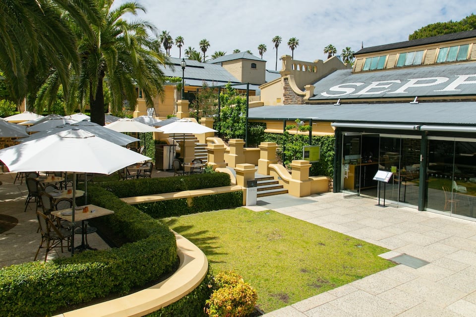 A courtyard with outdoor seating, palm trees, and a building with 'SEPP' on the roof.